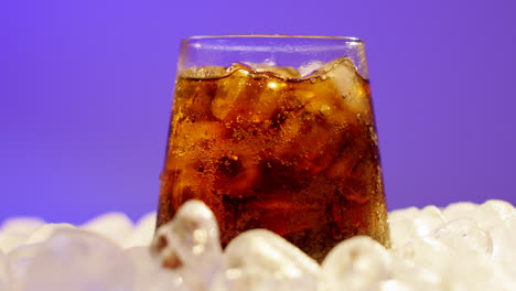 Nahaufnahme-Einer-Person,-Die-Ein-Gekühltes-Kaltgetränk-Im-Glas-Auf-Eiswürfeln-Vor-Violettem-Hintergrund-Aufnimmt